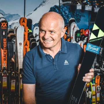 Manfred Rogetzer, the boss of the Bründl Sports Racing Service, with a pair of Fischer skis in his hands, standing in front of a wall of skis